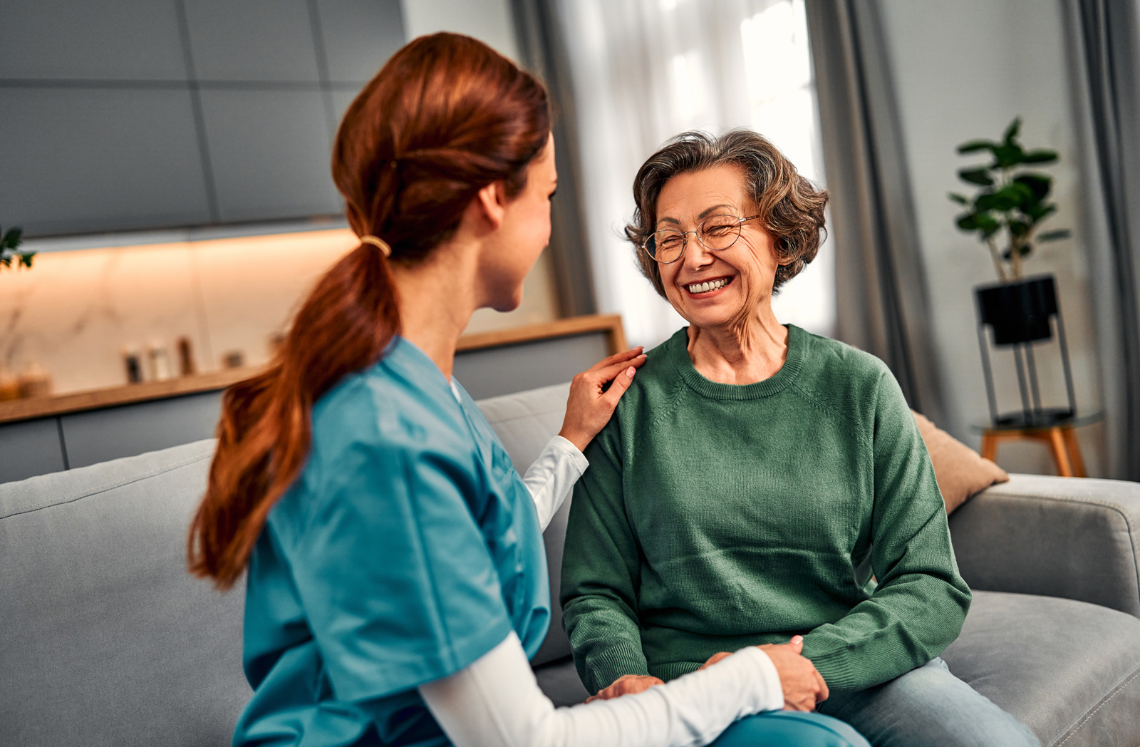 Caregiver comforting smiling elderly woman on couch