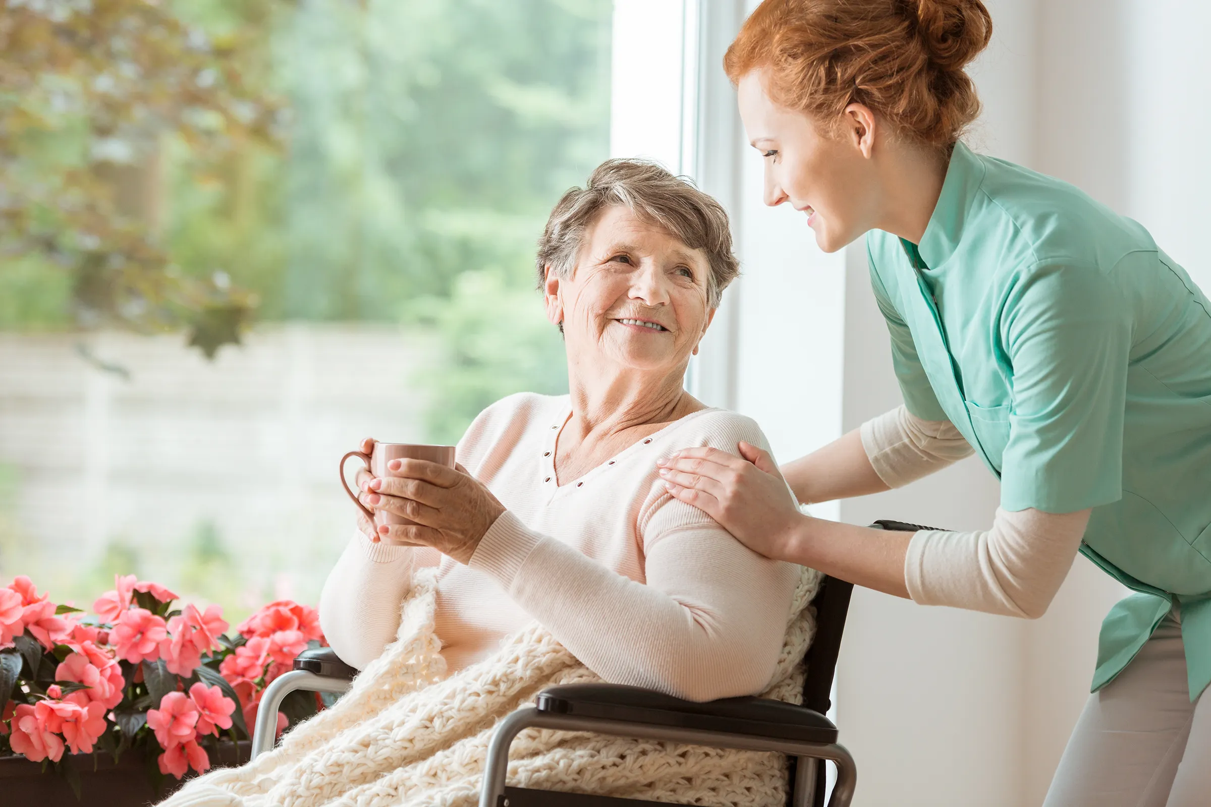 Caregiver assisting elderly woman in wheelchair indoors